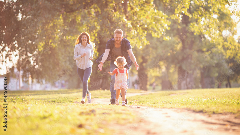 Fototapeta premium Young happy parents with their baby girl having fun outdoors