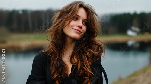 Beautiful young woman with long wavy hair smiling outdoors near a river on a cloudy day