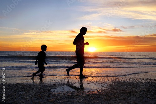 Silhouette of Father and his Young Son Jogging on Beach Together at Sunset