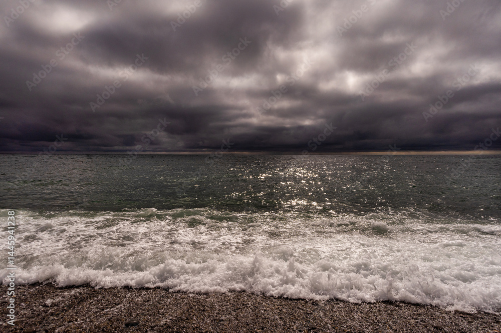 Sun between dark storm clouds over ocean. Dramatic seascape. Clouds and rain flurry over sea.