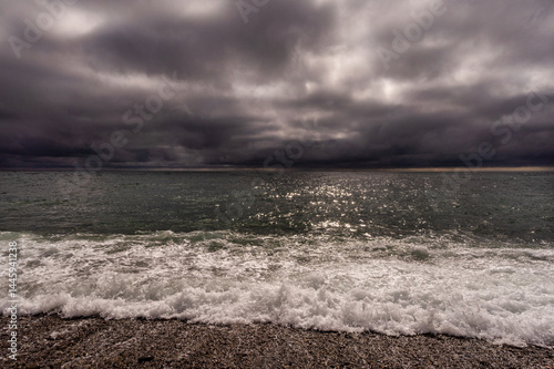 Obraz na płótnie Sun between dark storm clouds over ocean. Dramatic seascape. Clouds and rain flurry over sea. w salonie