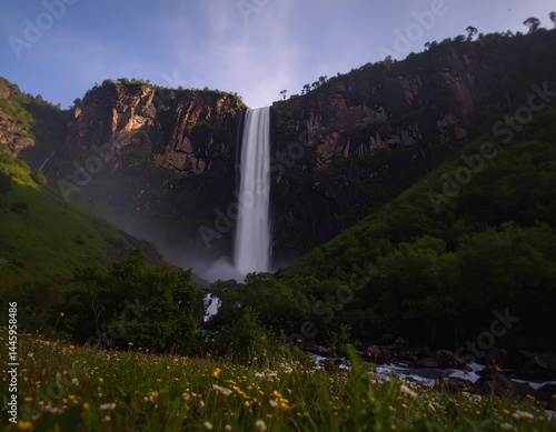 Un majestuoso paisaje montañoso captura la serena belleza de las cascadas que se desbordan por exuberantes laderas verdes. El agua centellea al caer sobre acantilados rocosos, rodeados de densa vegeta