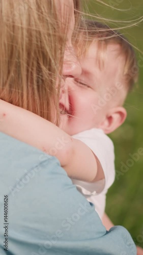 A woman in a blue dress bends down to embrace her son,who hugs her blissfully with a big smile on his face. tender moment of love and connection between mother and child in a sunny, green grass field