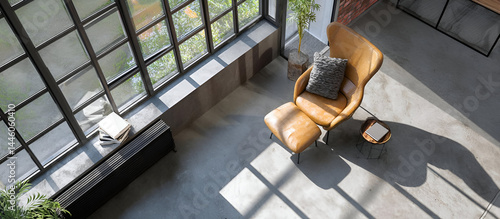 A cozy reading nook in an industrial apartment, large windows letting in natural light, polished concrete floors with a comfy armchair, captured from a top view.