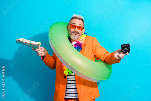 Cheerful mature man in orange suit, enjoying summer vacation vibe with inflatable ring, tropical accessories, and a colorful background