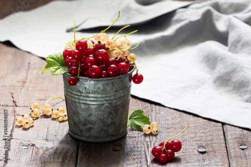 White and red currants in a metal bucket on a wooden background.