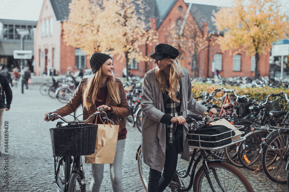 Obraz premium Young lesbian couple shopping and pushing their bicycles on a city street