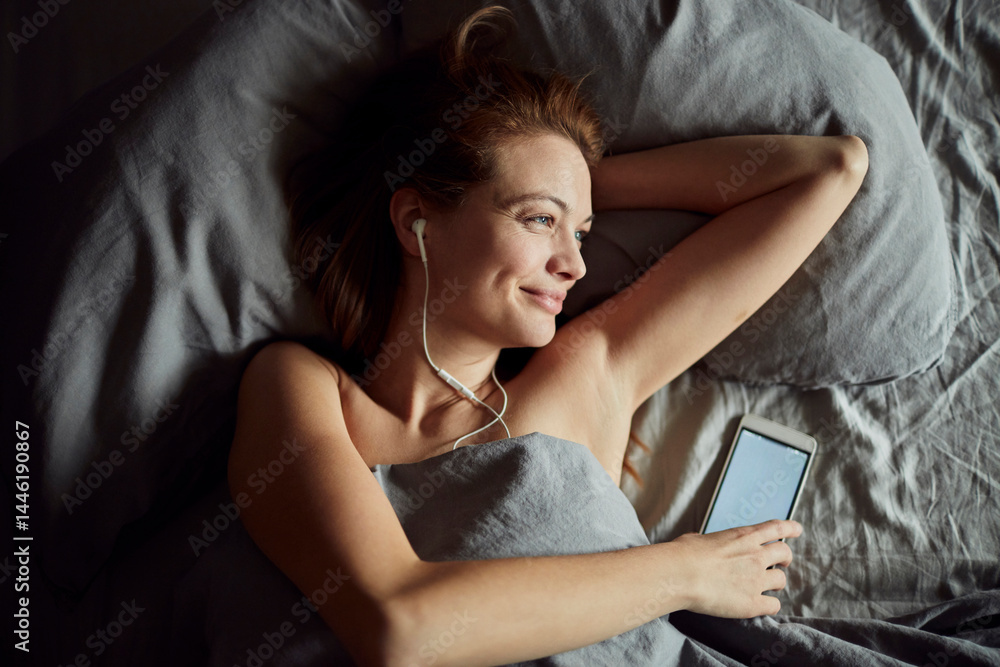Naklejka premium Young beautiful caucasian woman using a smart phone after waking up in the morning in her bed in a bedroom