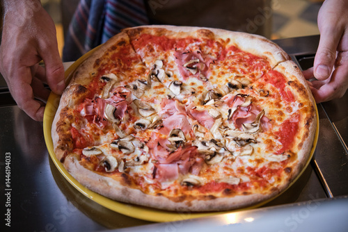 Chef placing delicious pizza with ham and mushrooms on metal counter