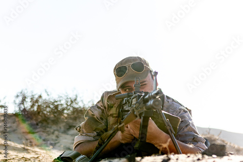 Soldier in desert camouflage aiming through rifle scope