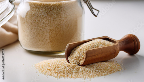 raw uncooked fonio seeds in a wooden scoop near glass jar on white table closeup african cereal