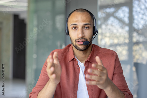 Obraz na płótnie A man wearing a headset gestures while looking directly at the camera. He seems to be in a video conference call, or an online meeting. w salonie