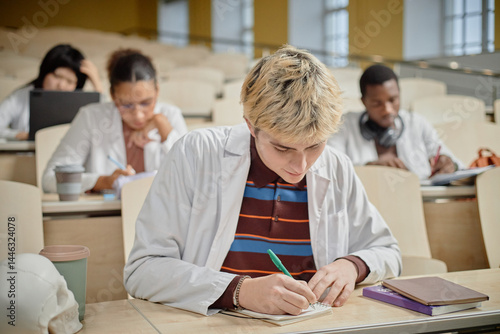 Side view portrait of young med student focusing and writing in notebook during class in lecture hall at college