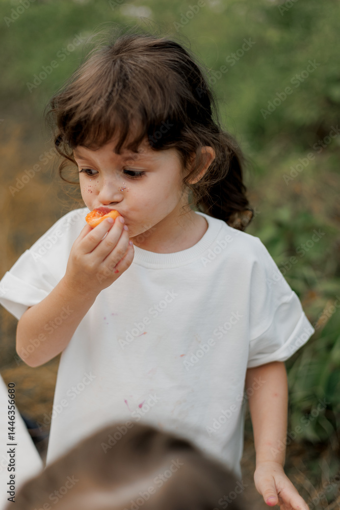 Fototapeta premium a stylish little girl appetizingly eats a delicious treat during a children's picnic in the evening in nature