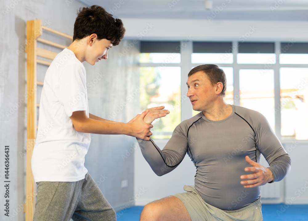 Obraz premium Adult man and boy teenager training self-defense techniques in studio