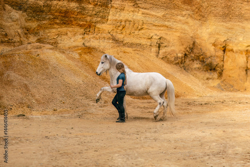 Obraz na płótnie A young woman and her white icelandic horse gelding interacting in a sand pit; horsemanship concept w salonie