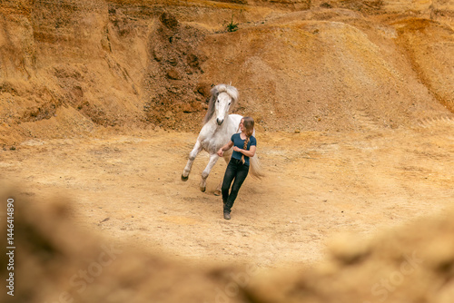 Obraz na płótnie A young woman and her white icelandic horse gelding interacting in a sand pit; horsemanship concept w salonie