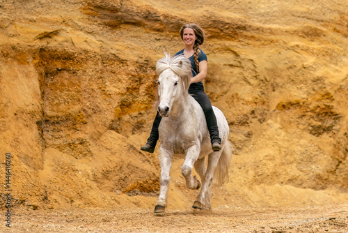 A young woman and her white icelandic horse gelding interacting in a sand pit; horsemanship concept