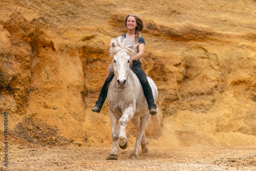 A young woman and her white icelandic horse gelding interacting in a sand pit; horsemanship concept