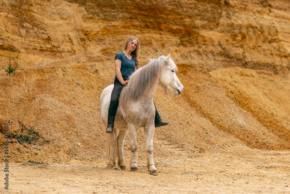 A young woman and her white icelandic horse gelding interacting in a sand pit; horsemanship concept