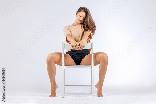 Young women posing with short shirt on a chair.