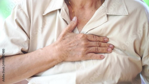 Elderly person wearing beige shirt with hand on chest showing discomfort and pain close up skin texture senior health concern