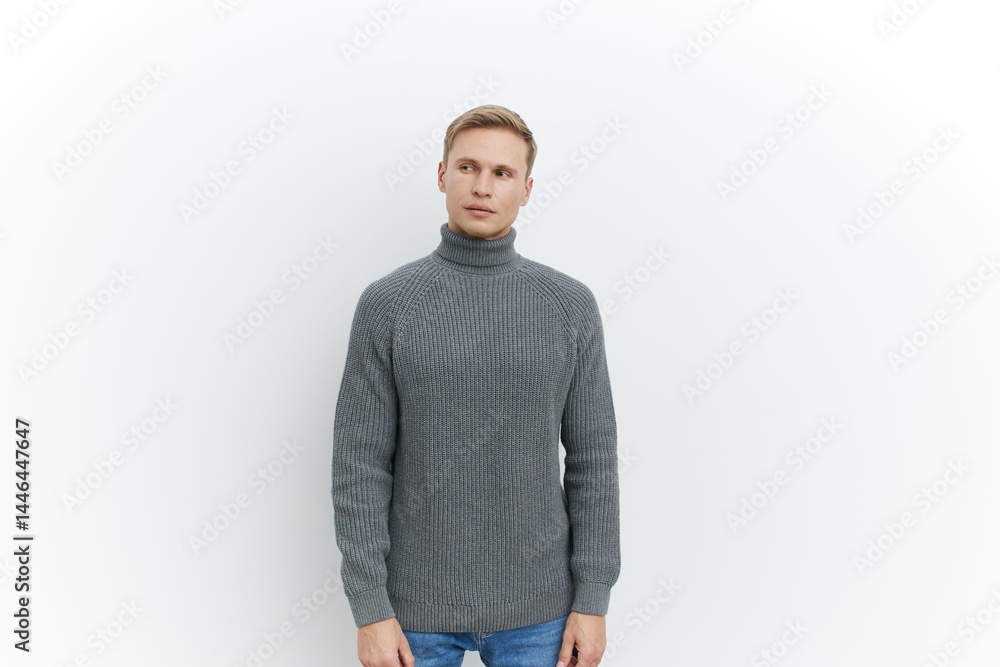 Fototapeta premium Full body portrait of a young Caucasian man with blonde hair wearing a gray knitted turtleneck sweater, looking at camera, standing against plain white background, studio shot, casual fashion, men