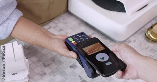 Mobile phone gently touching NFC terminal for contactless payment in slow and smooth motion, executed by customer in casual attire inside cozy cafe environment with soft lighting