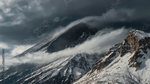A view of snow capped mountains partially covered by clouds under a dark and stormy sky in the wilderness