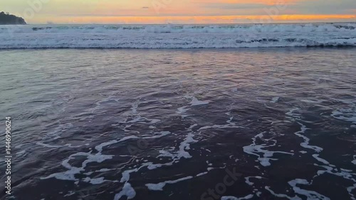 Crushing wave in sunset. Tide on the beach.From a distance seen the rolling and breaking of the sea waves,foam shaped wave current flows to the beach.
