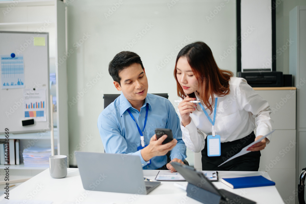 Fototapeta premium Two young Asian professionals engaged in teamwork and business discussions in modern office embodying corporate