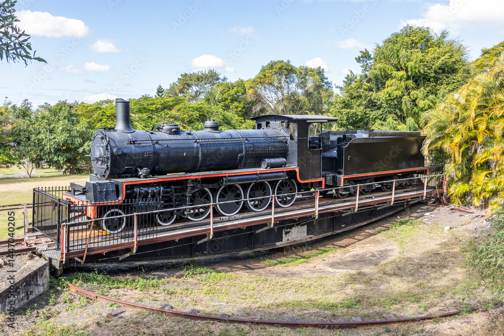 Fototapeta premium A retired old steam locomotive and coal truck on a turntable for turning trains around at the end of the line against a background of trees and sky at Imbil in Queensland, Australia.