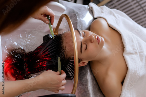 Close-up of a woman receiving a relaxing Japanese head spa treatment, with green massage sticks applied to her scalp, while water gently flows from a special tool during the session in a beauty salon