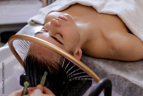 Close-up of a woman receiving a relaxing Japanese head spa treatment, with green massage sticks applied to her scalp, while water gently flows from a special tool during the session in a beauty salon