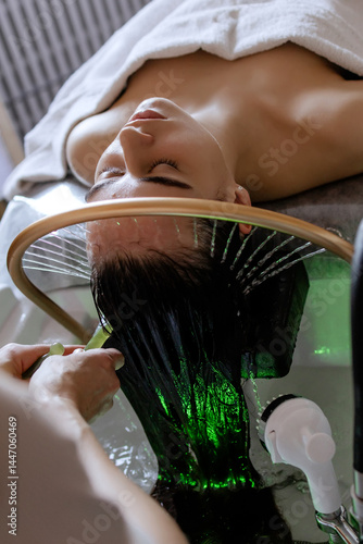Close-up of a woman receiving a relaxing Japanese head spa treatment, with green massage sticks applied to her scalp, while water gently flows from a special tool during the session in a beauty salon