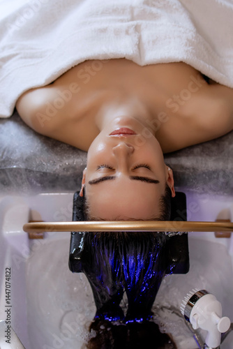 Close-up of a woman receiving a head massage during a Japanese head spa treatment with water flowing from a special hair washing tool, focusing on the scalp relaxation and beauty therapy