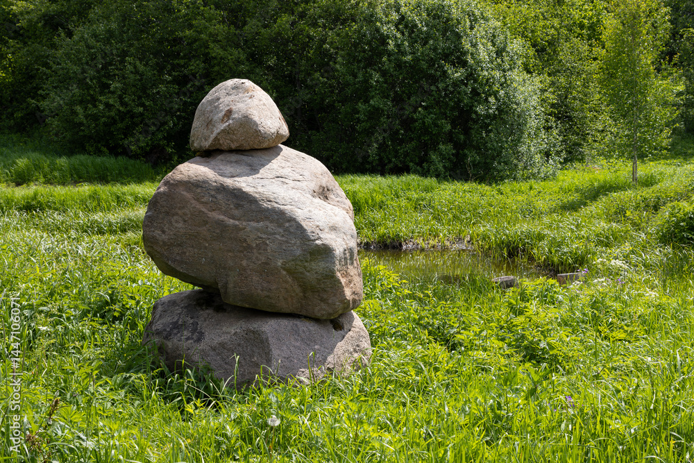 Stone pyramid made of large boulders. Stones among the grass. Tower of three large stones. Countryside. Tourist attraction.