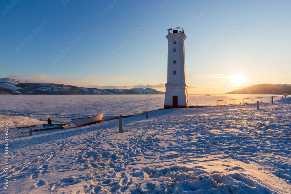 Leading beacon on the snowy shore of the sea bay. Evening winter landscape. Beautiful sunset over the frozen sea. Nagaev Bay, Sea of Okhotsk. Park Mayak, Magadan, Magadan region, Far East of Russia.