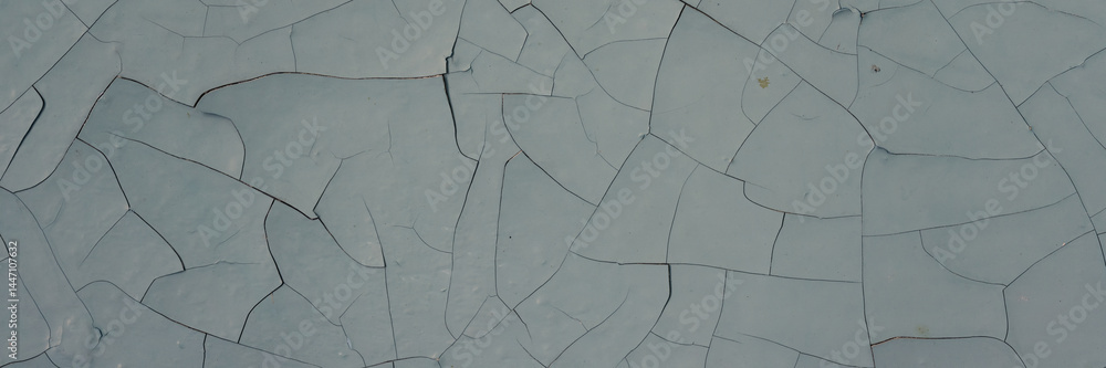 Peeling paint on the wall. Panorama of a concrete wall with old cracked flaking paint. Weathered rough painted surface with patterns of cracks and peeling. Panoramic texture for background and design.