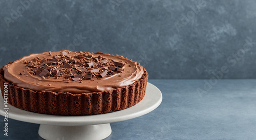 Decadent Chocolate Tart with Chocolate Shavings on Cake Stand against Blue Background with copy space