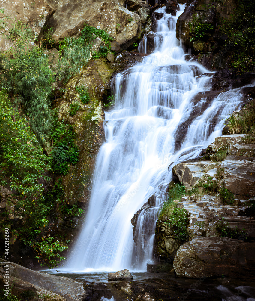 Obraz premium A breathtaking view of a cascading waterfall nestled in a lush, green forest. The water flows gracefully over rugged rocks and boulders, creating a serene and tranquil atmosphere.