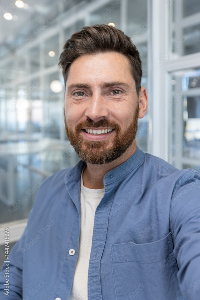 A smiling, bearded man in a blue shirt poses for a headshot indoors, showcasing his friendly and approachable demeanor. A smiling, bearded man in a blue shirt poses for a headshot indoors, showcasing his friendly and approachable demeanor.