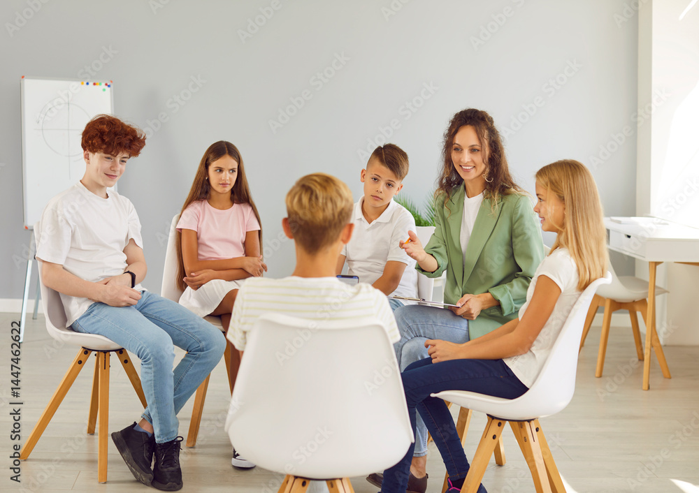 Friendly young school psychologist woman having conversation with a group of cute children sitting in a circle in classroom. Psychological support for kids and mental health concept.