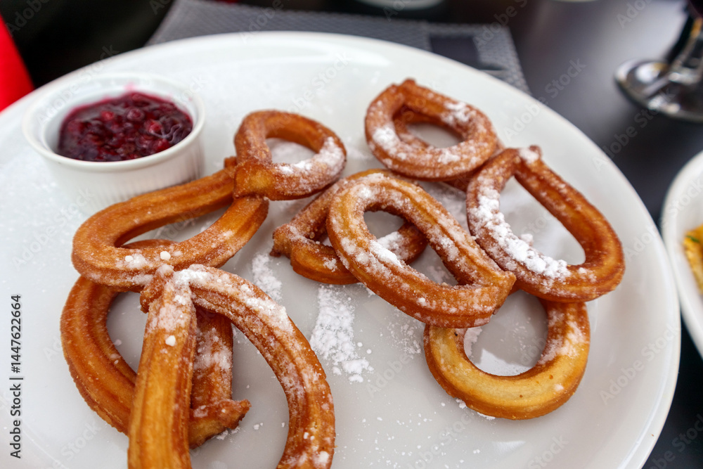 a plate with several golden brown churros sprinkled with powdered sugar and a small white dish with dark berry sauce.
a plate with several golden brown churros sprinkled with powdered sugar and a small white dish with dark berry sauce.