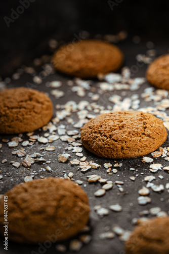 Craft and rustic four oatmeal cookies. Dark food aesthetics, black background with several oat flakes.