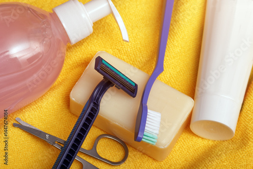 The personal hygiene set on yellow towel background. Shampoo, scissors, razor, soap and toothbrush for everyday care.