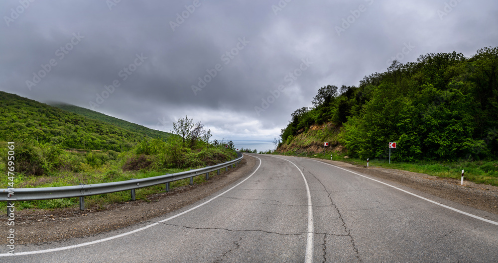 Road Trip the Hill to the Sea. Empty long mountain road to the horizon on a sunny summer day with dramatic cloudy sky. Highway turn panoramic view. Woods rural freeway. Traffic background.