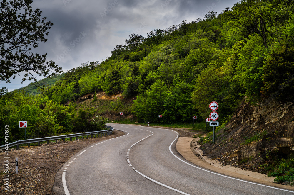 Road Trip the Hill to the Sea. Empty long mountain road to the horizon on a sunny summer day with dramatic cloudy sky. Highway turn panoramic view. Woods rural freeway. Traffic background.