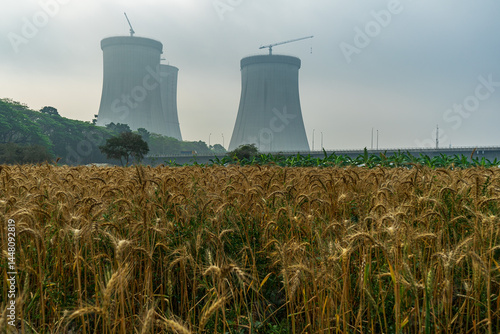 Obraz na płótnie Cooling towers of nuclear power plant rising behind field of ripe wheat. industrial infrastructure with nature under a cloudy sky, contrast between agriculture and industry. w salonie