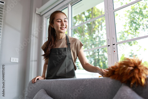 Konstfotografi A confident young woman stands in a clean kitchen, proudly holding cleaning supplies, smiling as she works with expertise and pride in her job
